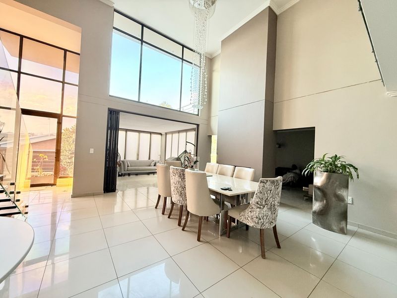 Spacious open-plan dining area featuring double-volume ceilings, large floor-to-ceiling windows, polished tile flooring, and a modern crystal chandelier.
