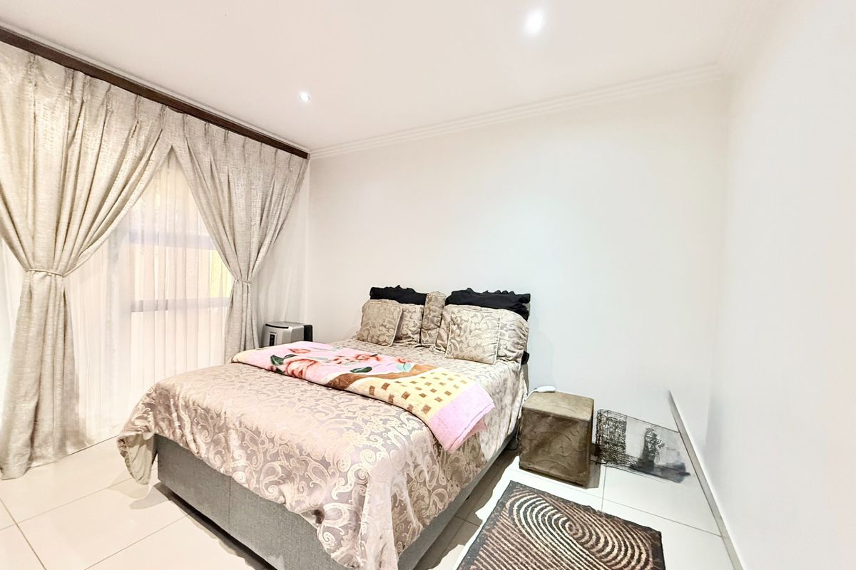 A bright bedroom featuring tiled flooring, recessed ceiling lighting, and large sliding glass doors with elegant curtains.