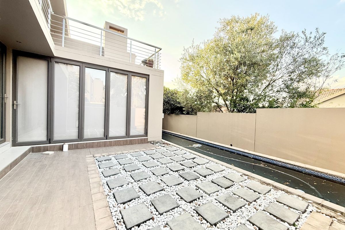 A rear patio area featuring tiled flooring, a stone-paved garden section, and a swimming pool, complemented by a balcony above with metal railings.