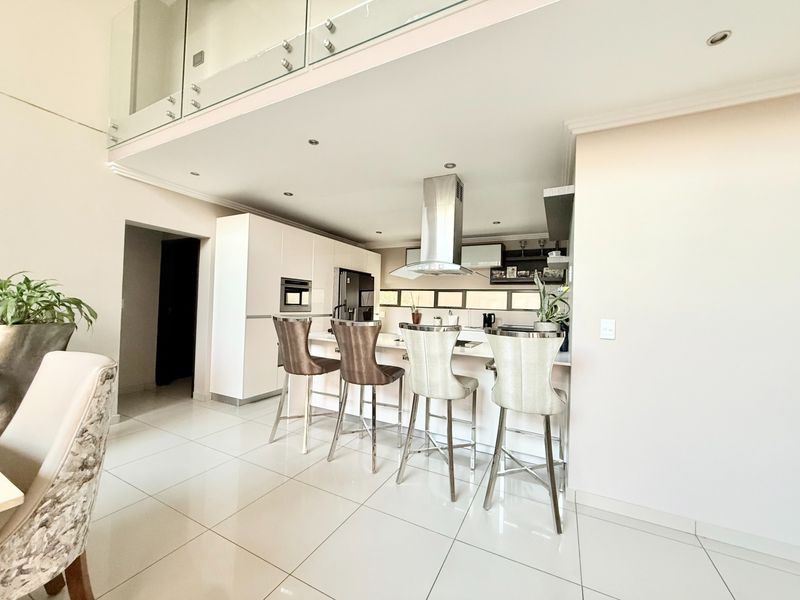Modern open-plan kitchen featuring a central island with breakfast bar seating, stainless steel extractor fan, and sleek cabinetry with integrated appliances.