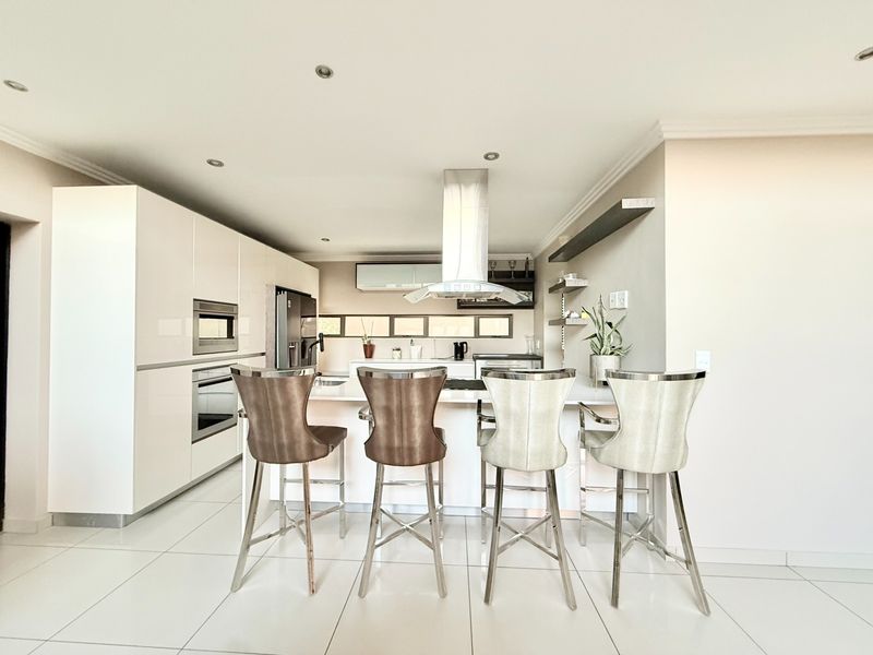 Modern kitchen featuring high-gloss cabinetry, a central island with breakfast bar seating, stainless steel extractor fan, and integrated oven and microwave.