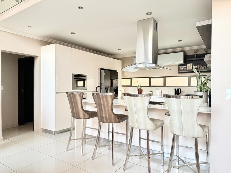 Modern kitchen featuring high-gloss cabinetry, a central island with breakfast bar seating, built-in oven, and a stainless steel extractor fan.