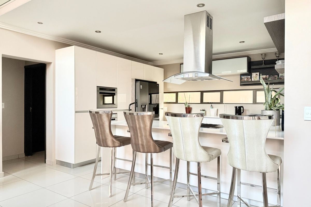 Modern kitchen featuring high-gloss cabinetry, a central island with breakfast bar seating, built-in oven, and a stainless steel extractor fan.