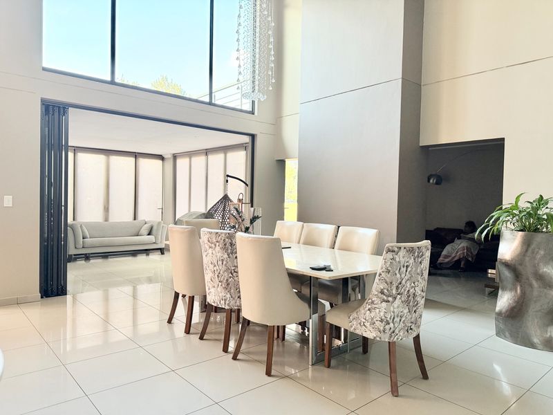 Spacious open-plan dining area featuring double-volume ceilings, large windows, and seamless flow to an adjacent lounge and outdoor patio area.