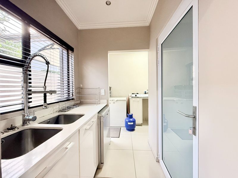 A functional scullery area featuring a double sink, modern gooseneck faucet, white cabinetry, and tiled flooring, with an adjacent utility space visible.