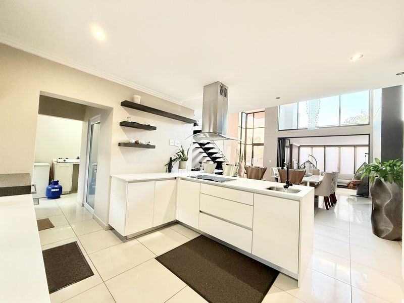 Modern open-plan kitchen featuring a central island with integrated hob, stainless steel extractor fan, sleek cabinetry, and adjacent scullery area.