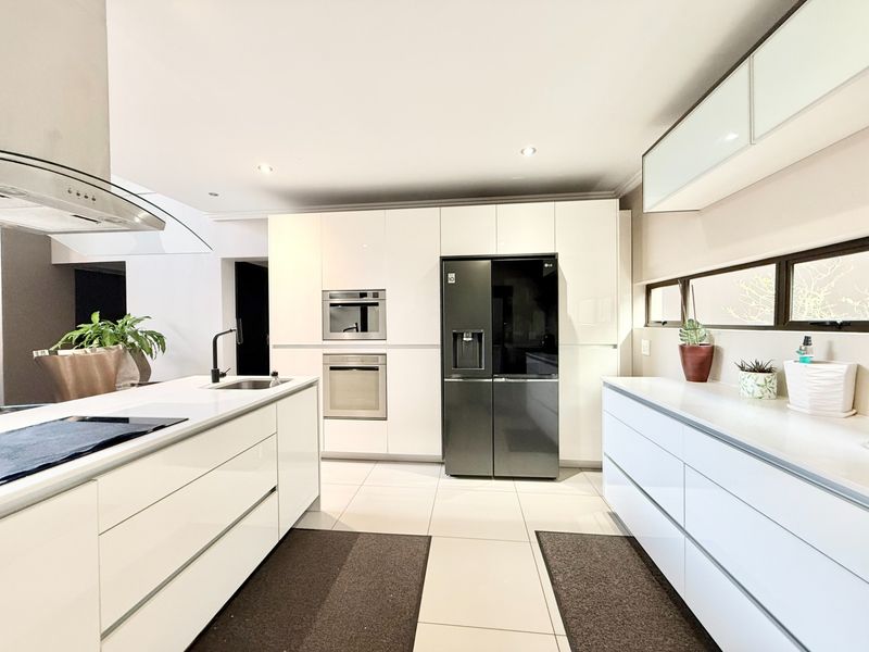Modern kitchen featuring high-gloss white cabinetry, stone countertops, a central island with integrated sink, and built-in stainless steel oven and microwave.