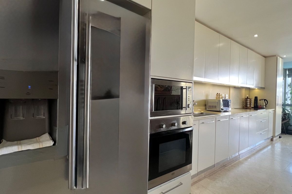 Modern kitchen featuring sleek cabinetry, integrated stainless steel appliances, built-in oven and microwave, and polished stone flooring with direct access to an outdoor area.
