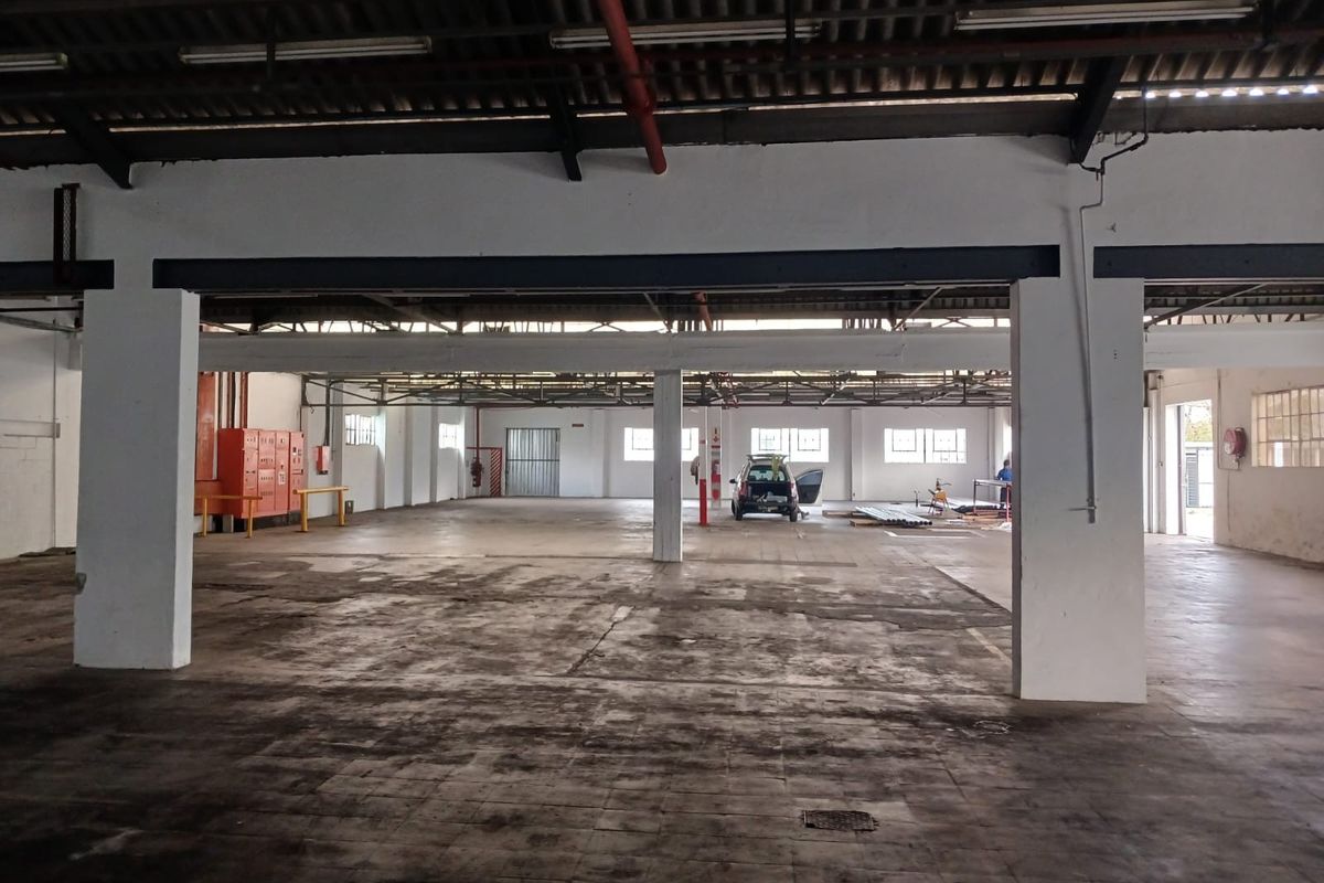 Spacious industrial warehouse area featuring high ceilings, exposed structural beams, concrete flooring, and integrated fire safety equipment.