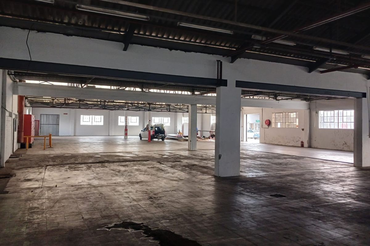 Spacious industrial warehouse featuring high ceilings, exposed steel trusses, concrete flooring, and large windows providing ample natural light.