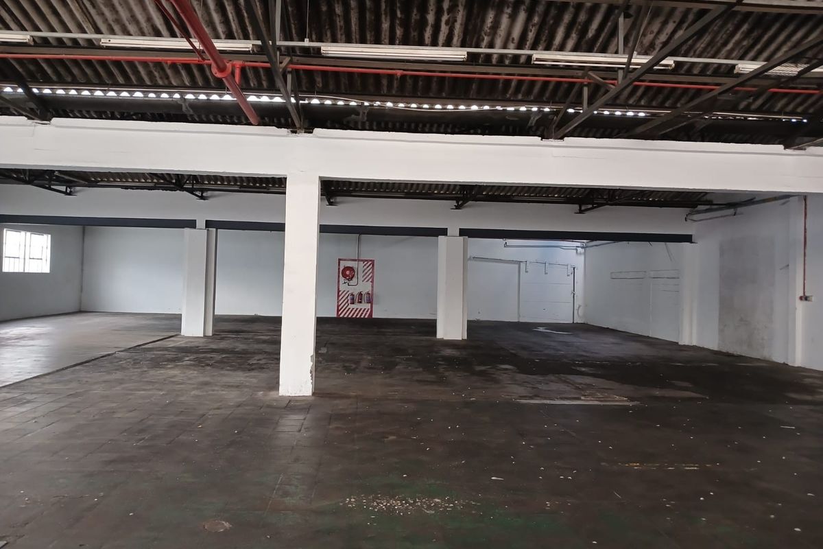 Spacious industrial warehouse area featuring high ceilings, exposed structural beams, concrete flooring, and integrated fire safety equipment.