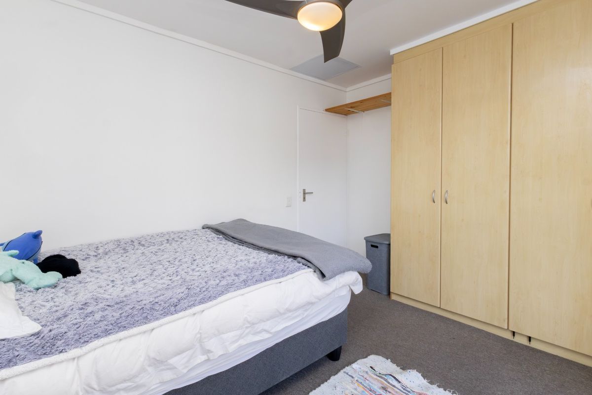 A functional bedroom featuring neutral walls, carpeted flooring, a ceiling fan, and built-in wooden wardrobes for storage.