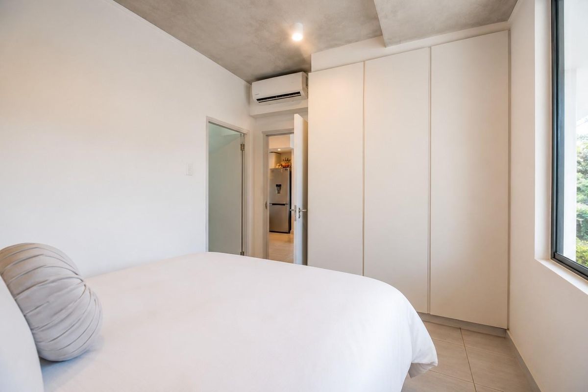 Modern bedroom featuring built-in wardrobes, split-system air conditioning, tiled flooring, and an exposed concrete ceiling with a view through the window.
