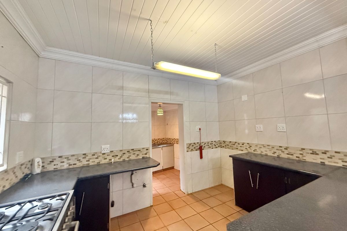 A functional kitchen featuring dark cabinetry, laminate countertops, tiled splashbacks, and a gas stove, with an adjoining scullery area.
