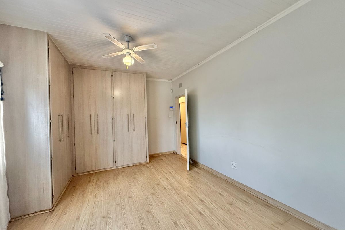 A bright, empty bedroom featuring light-toned laminate flooring, built-in cupboards, and a ceiling fan, offering a clean canvas for personalization.