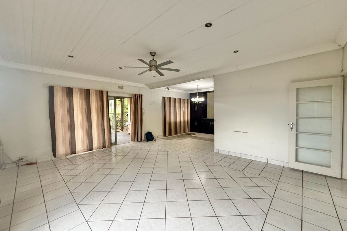 Spacious, empty living area featuring tiled flooring, a timber panelled ceiling with a fan, and direct access to an outdoor patio area.