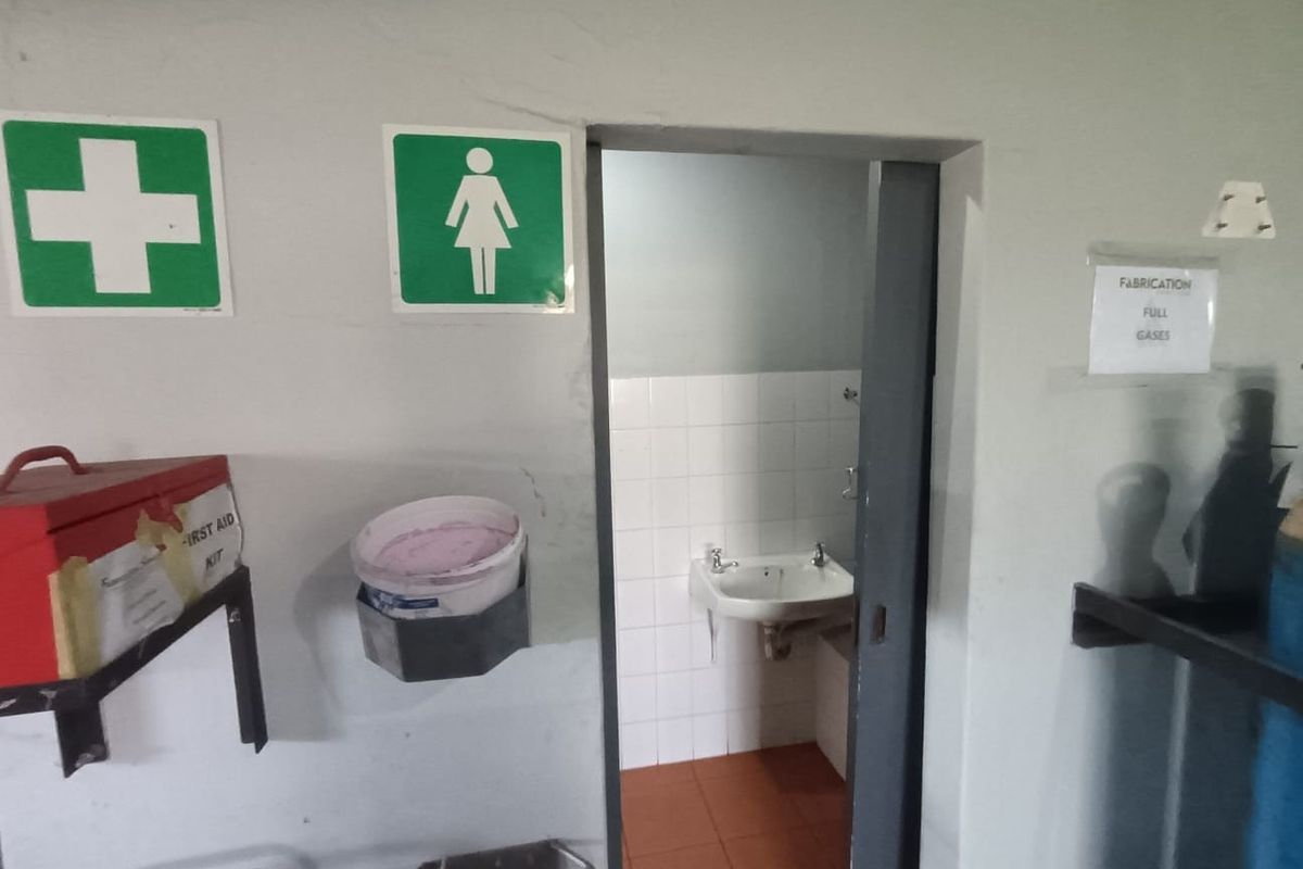 A functional commercial restroom facility featuring a wall-mounted basin with tiled splashback and durable tiled flooring, accessed via a sliding door.