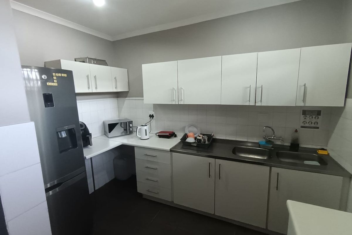 A functional kitchen area featuring white built-in cabinetry, a double stainless steel sink, tiled backsplash, and dark floor tiles.