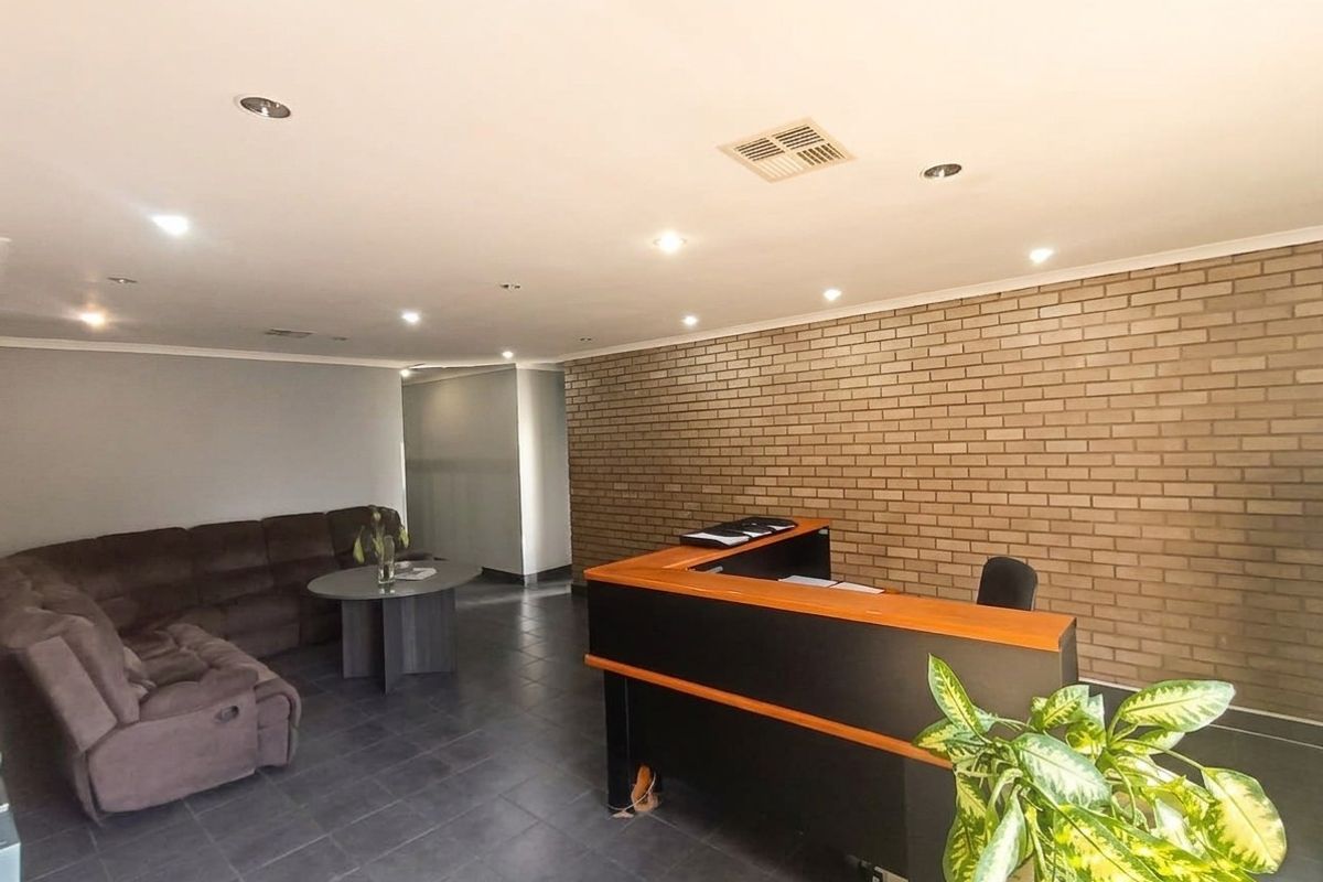 A professional commercial office reception area featuring a built-in reception desk, recessed lighting, and a feature brick wall with durable tiled flooring.
