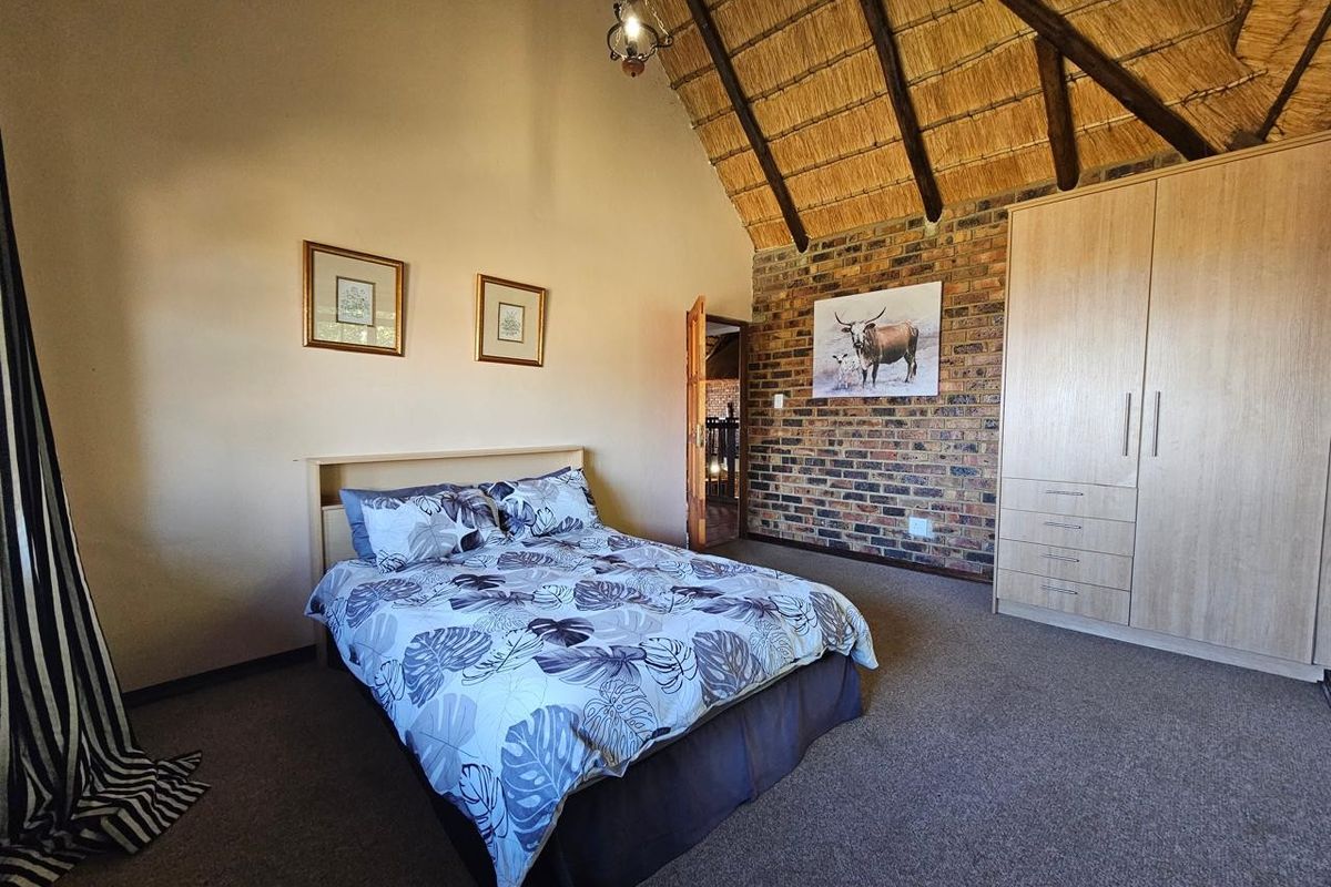 A spacious bedroom featuring a high thatched ceiling with exposed timber rafters, an exposed brick feature wall, and a built-in wardrobe.