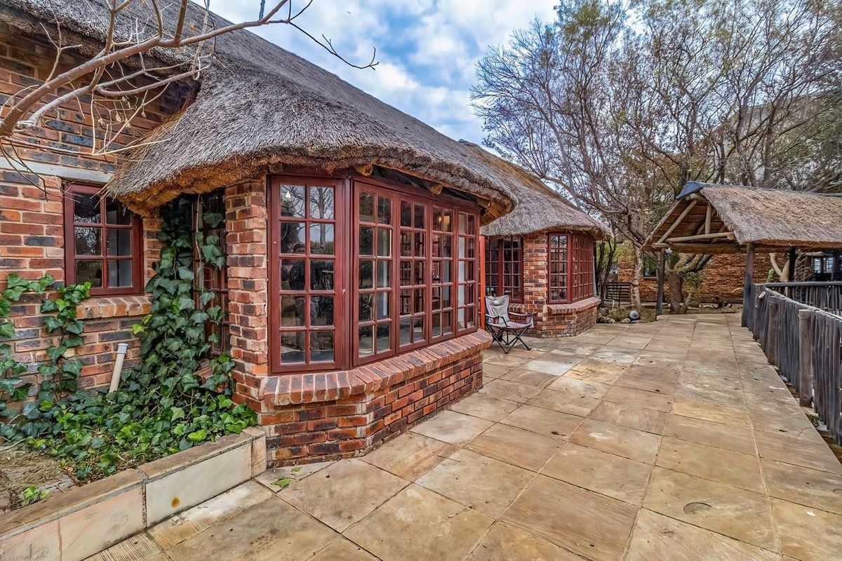 Rear exterior view featuring a traditional thatched roof, exposed brickwork, bay windows, and a spacious stone-paved patio area.