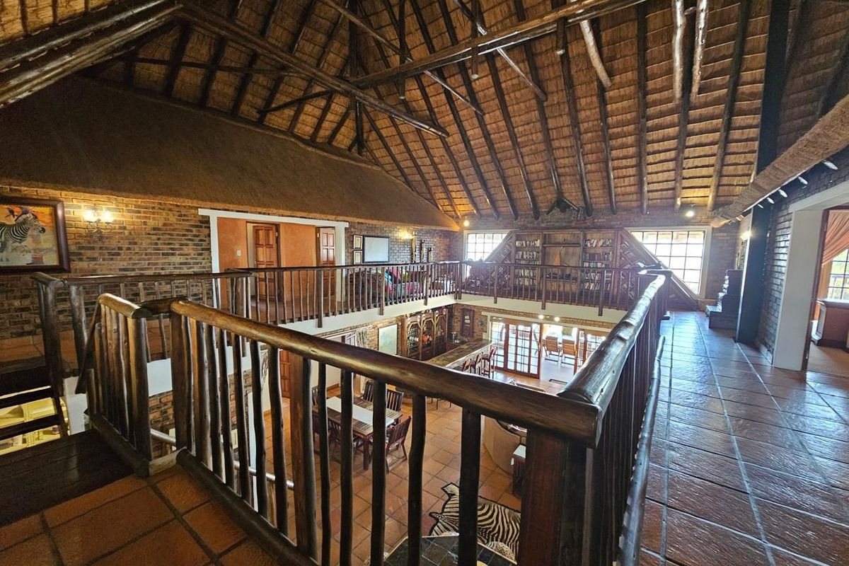 Spacious open-plan living area featuring a dramatic high-pitched exposed thatch roof, timber trusses, exposed brickwork, and a mezzanine level overlooking the main floor.