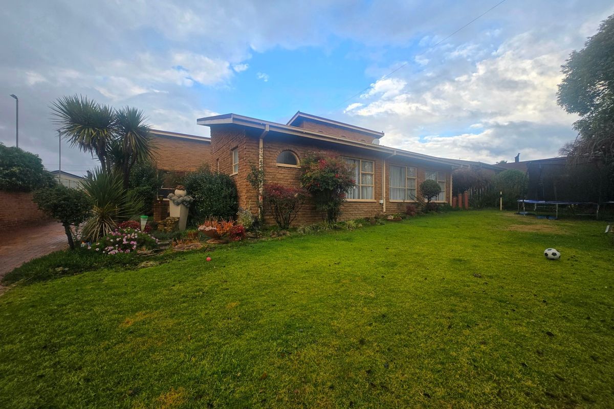 A view of the rear brick facade of the house, featuring large windows and a well-maintained lawn area.