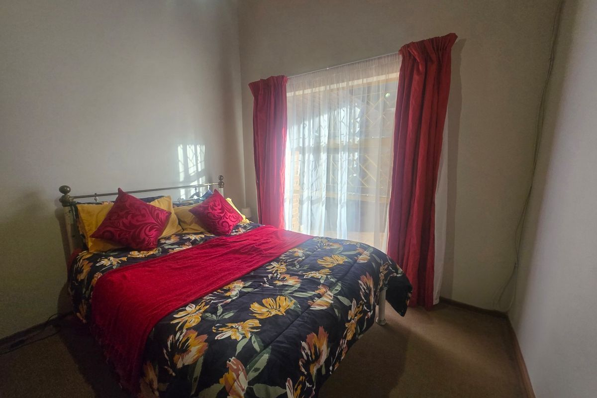A standard bedroom featuring carpeted flooring and a window fitted with a security gate.