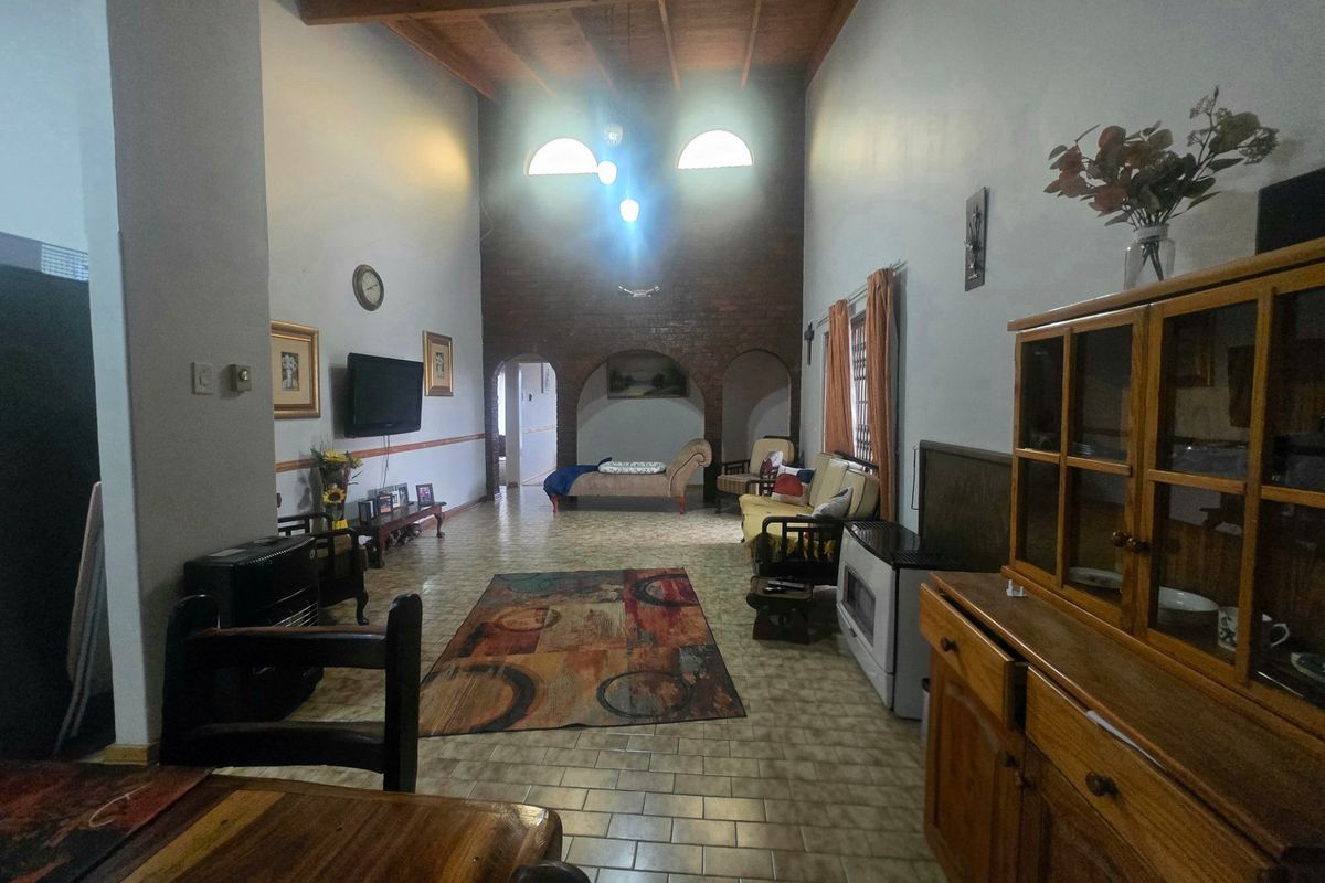 Spacious living area featuring high ceilings with exposed timber beams, a brick feature wall, and arched architectural details.