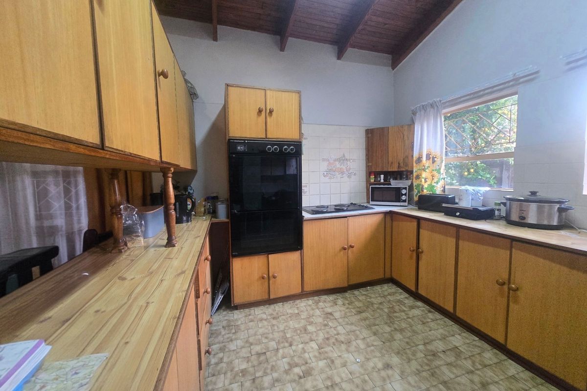 A dated kitchen featuring original wooden cabinetry, laminate countertops, built-in oven and hob, and exposed timber ceiling beams.