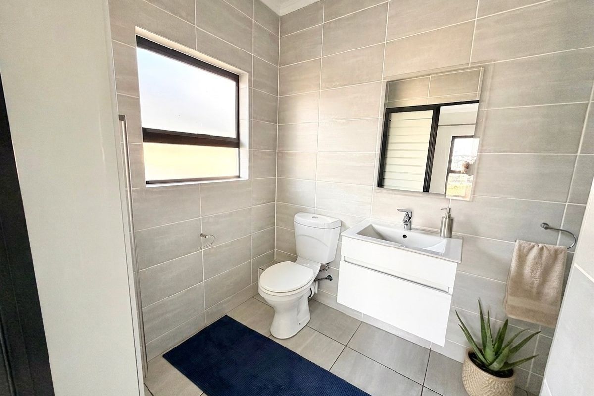 Modern bathroom featuring neutral wall tiles, a wall-mounted vanity with a basin, and a toilet.