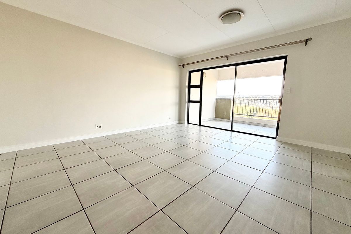A bright, empty living room featuring neutral tiled flooring and a large sliding glass door providing access to an outdoor balcony.