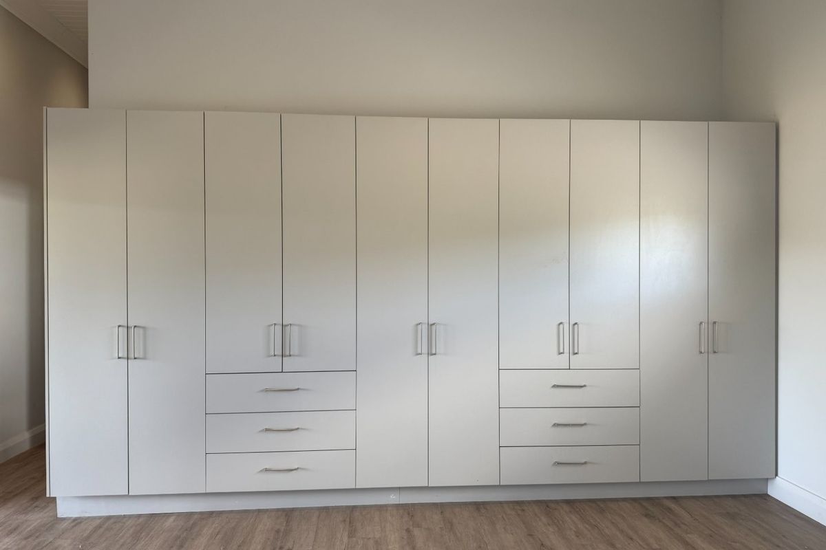A spacious bedroom featuring extensive floor-to-ceiling built-in cupboards with modern finishes and durable laminate flooring.