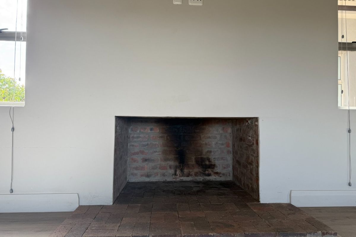 A minimalist living room featuring a central brick fireplace with a matching brick hearth, flanked by two windows and finished with neutral walls.