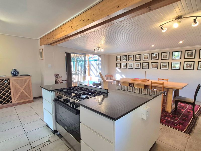 Spacious open-plan living and dining area featuring a central kitchen island with gas cooktop, exposed timber beams, and direct access to the outdoor patio.