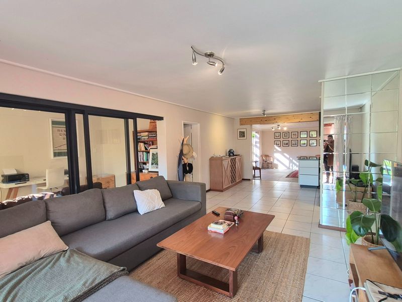 Spacious open-plan living area featuring tiled flooring, a modern sliding glass partition, and a decorative mirrored wall, creating a bright and versatile living space.