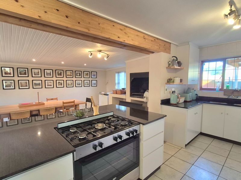 Spacious open-plan kitchen and dining area featuring a gas cooktop, granite countertops, exposed timber beam, and a built-in fireplace.