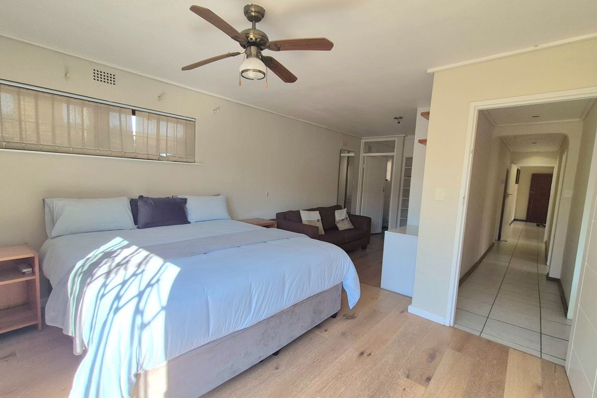 Spacious bedroom featuring light laminate flooring, a ceiling fan, and direct access to a tiled hallway.