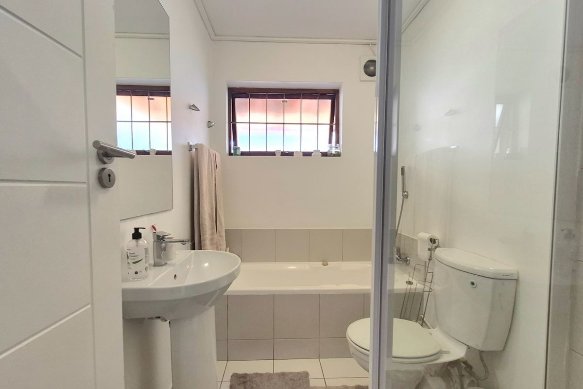 A clean and functional bathroom featuring a pedestal basin, built-in bathtub, separate shower enclosure, and toilet with neutral tiling.
