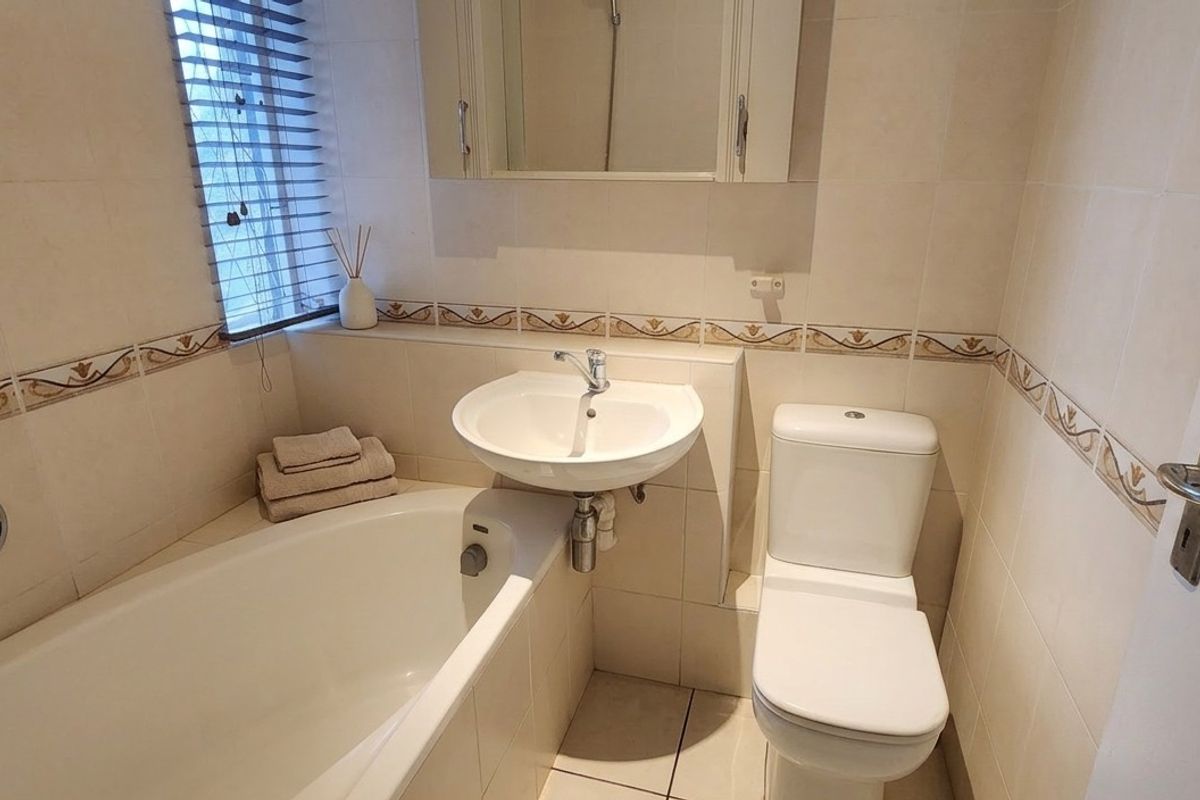 A functional bathroom featuring a bathtub, wall-mounted basin, toilet, and tiled finishes, providing a clean and practical space.