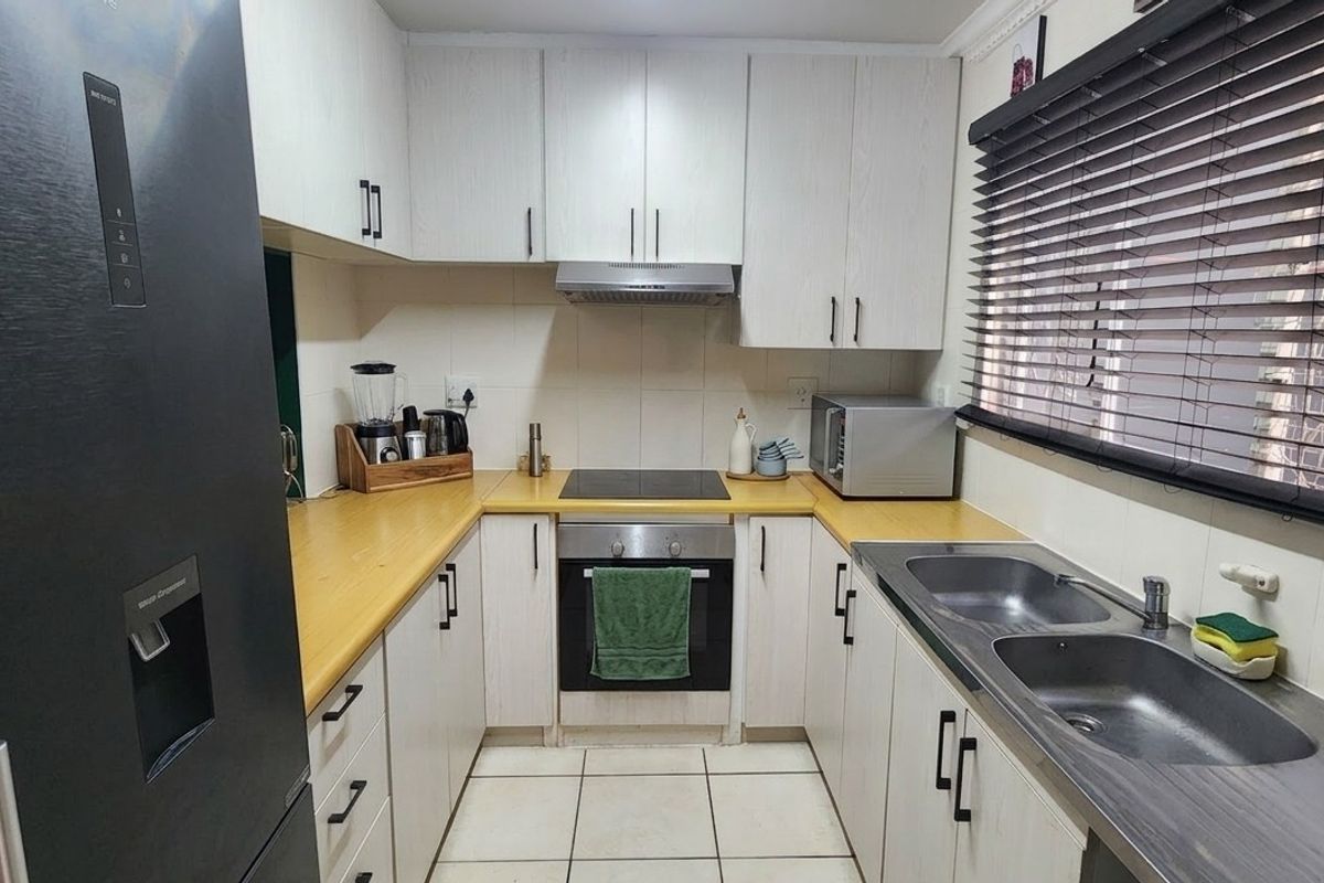 A functional U-shaped kitchen featuring light-toned cabinetry, laminate countertops, integrated oven and hob, and a double stainless steel sink with tiled flooring.