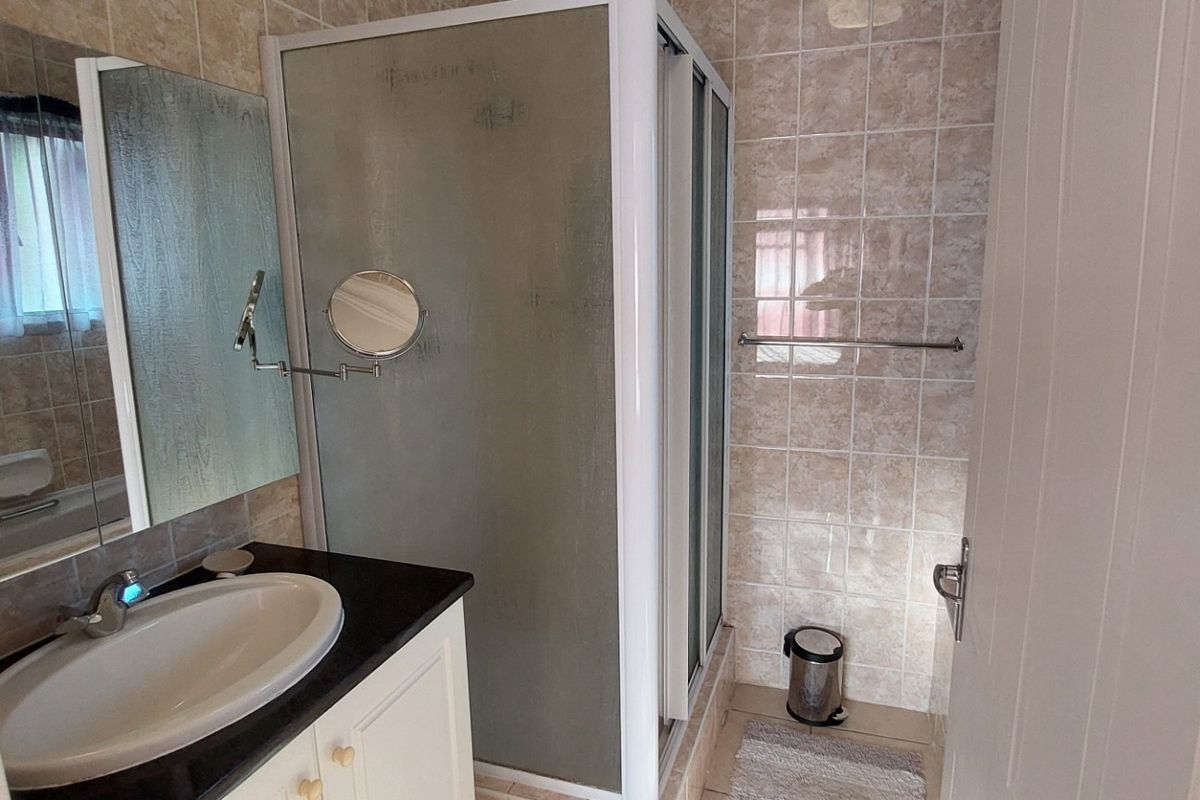 A functional bathroom featuring a vanity cabinet with an integrated sink, a shower enclosure, and neutral wall tiling.