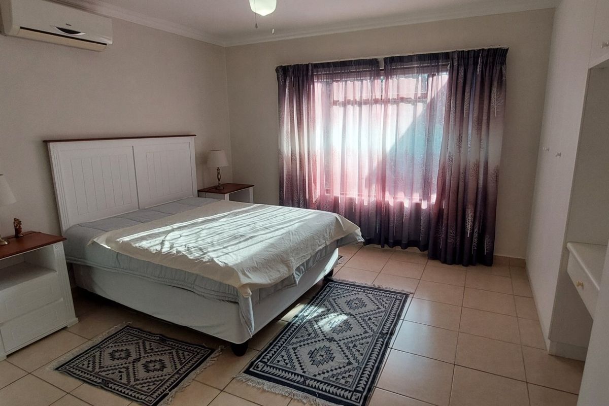 Spacious bedroom featuring tiled flooring, built-in cupboards, and a wall-mounted air conditioning unit.