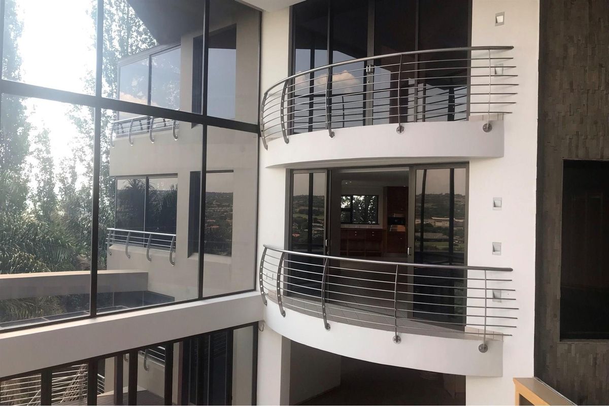 Modern multi-story commercial building facade featuring curved balconies with stainless steel railings and extensive glass curtain walling.