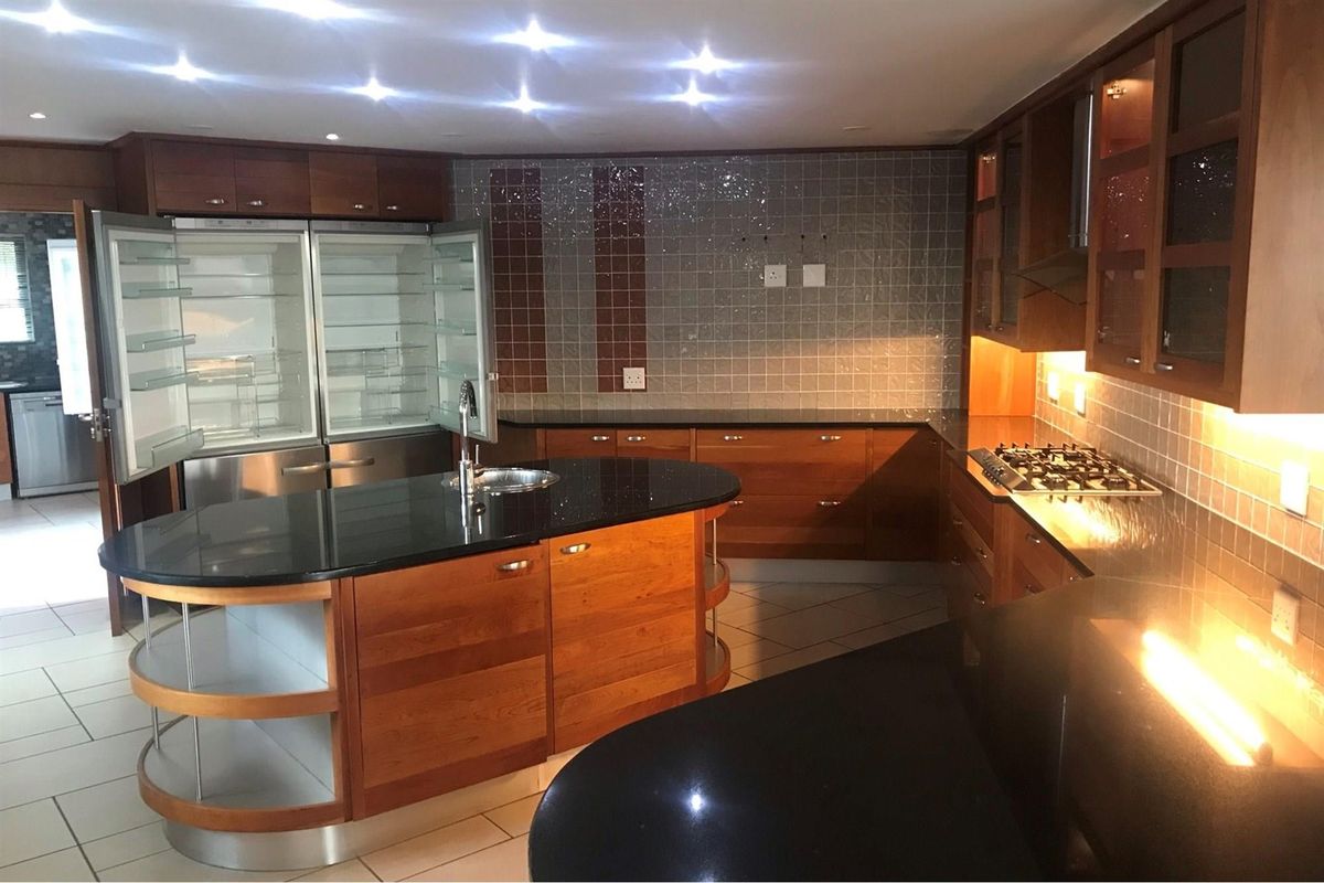 Spacious kitchen featuring dark granite countertops, extensive wooden cabinetry, a central island with a sink, and integrated gas hob with extractor fan.