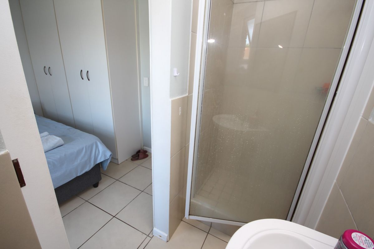 En-suite bathroom featuring a glass-enclosed shower and tiled flooring, conveniently adjacent to a bedroom with built-in cupboards.