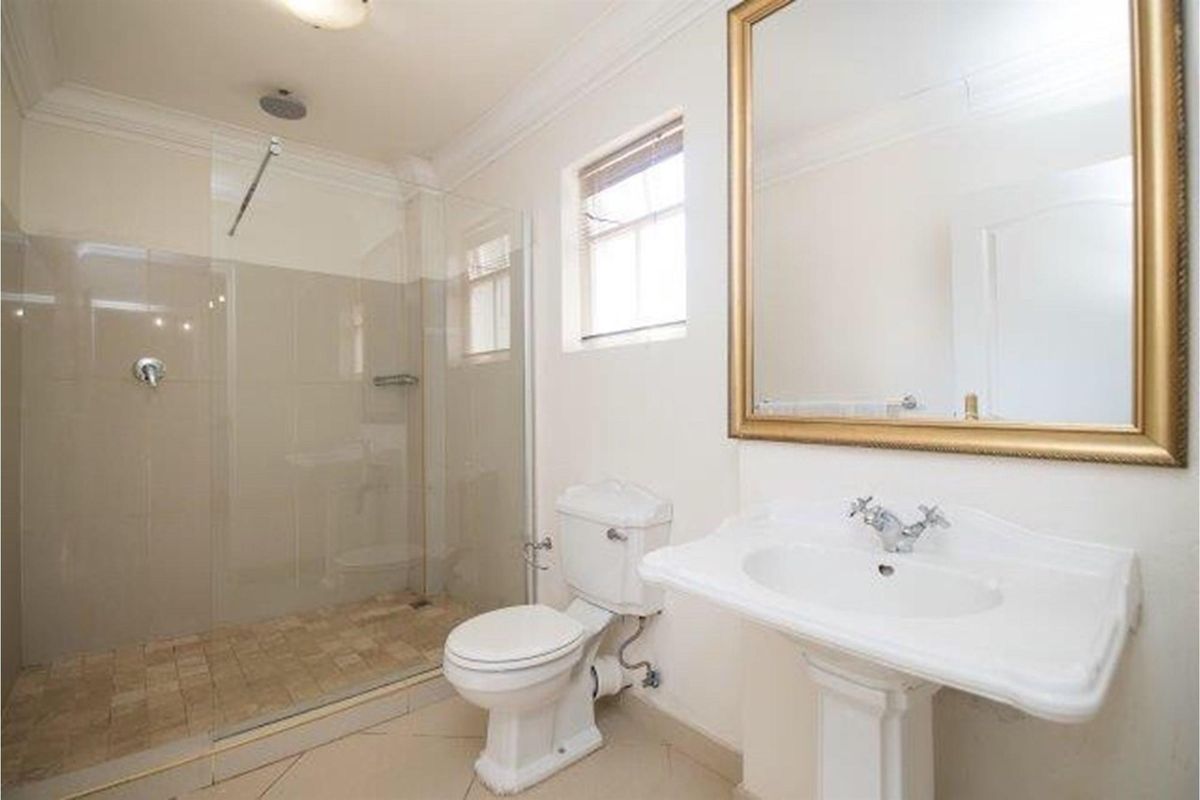 A clean and functional bathroom featuring a walk-in shower with glass screen, pedestal basin, and toilet with neutral tiled flooring.