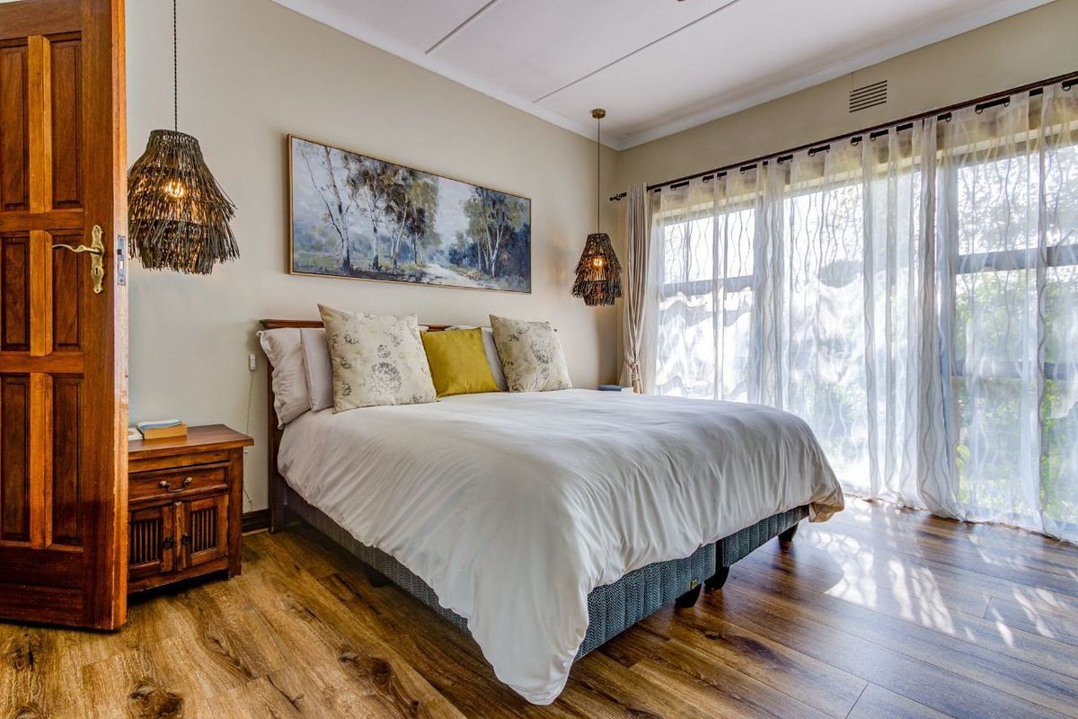 A well-maintained bedroom featuring warm laminate flooring, a timber door, and large sliding glass doors that provide ample natural light.