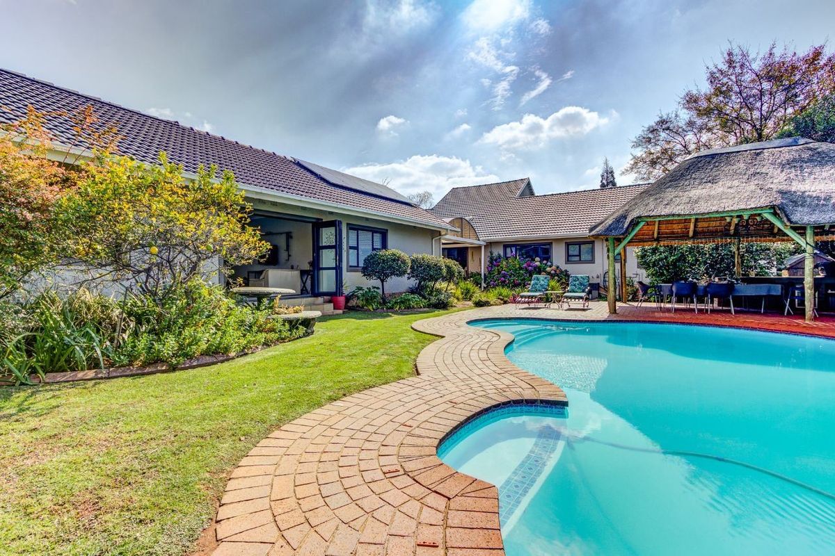 A well-maintained rear garden featuring a swimming pool, brick paving, and a traditional thatched lapa, perfect for outdoor entertaining.