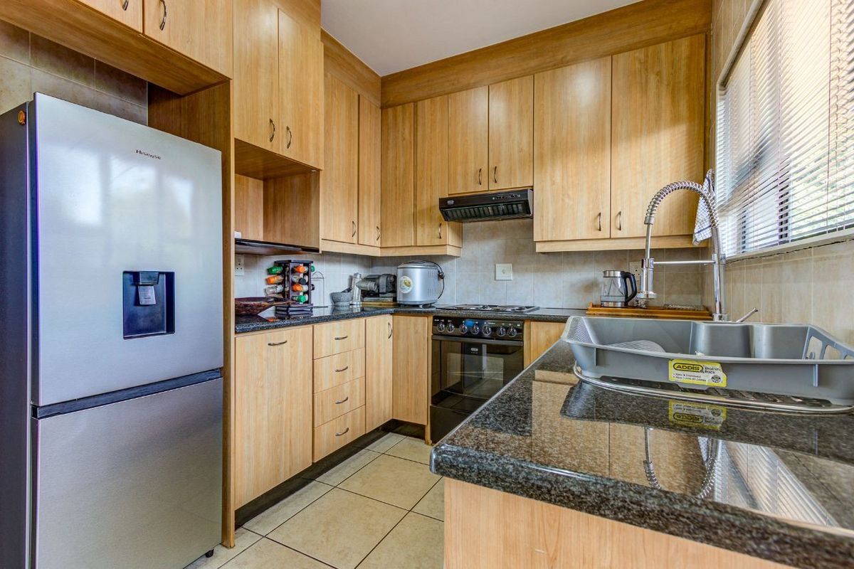 A functional kitchen featuring light wood-finish cabinetry, dark granite countertops, a built-in oven with extractor fan, and tiled flooring.